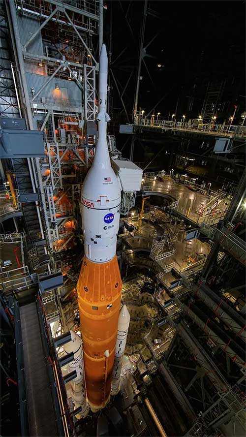 ten-lua-sls Hình ảnh tên lửa SLS với tàu vũ trụ Orion (màu trắng) gắn trên đỉnh, tại Tòa nhà Lắp ráp Phương tiện (VAB).
